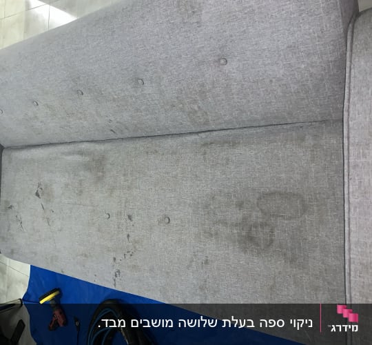 ספת בד אפורה עם כתמים וציוד ניקוי מקצועי לפני ניקוי